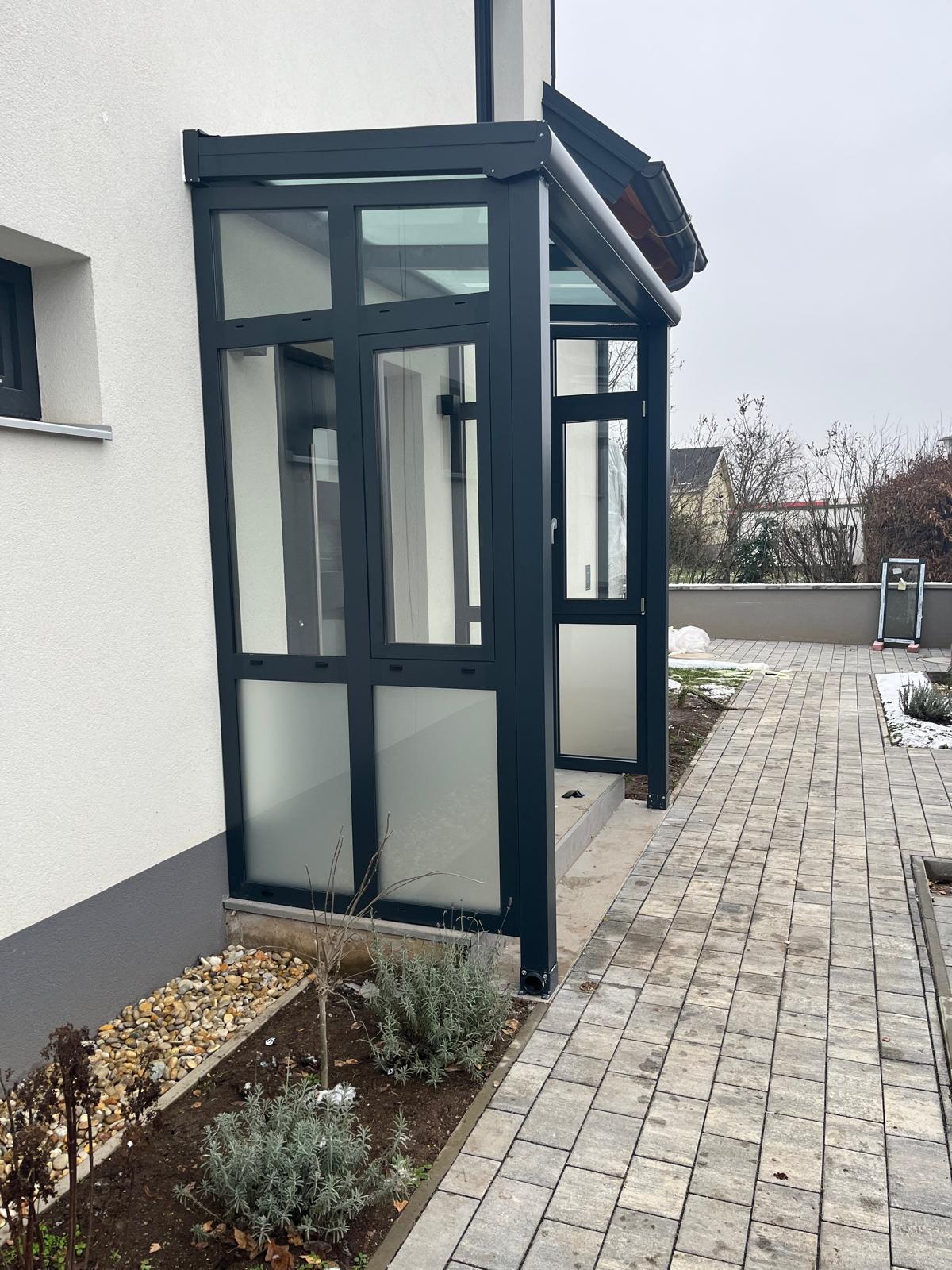 Anthrazitfarbener Windfang mit Glaselementen an weißer Hausfassade